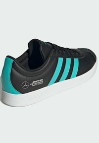Sort sneaker med turkise tre striber, hvid sål og en tekstureret læderoverflade. Har AMG Petronas-logo på siden.