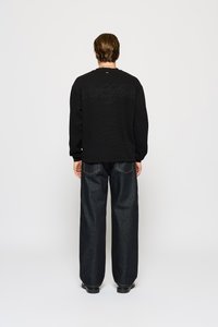 Sweatshirt noir texturé avec un logo en relief discret au dos, associé à un pantalon en denim foncé ample et des bottes noires.