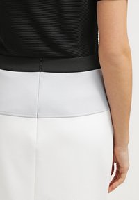 Černý žebrovaný top s hladkým černým páskem, kombinovaný s přiléhavou bílou sukní s lehce šedým panelem na zadní straně.