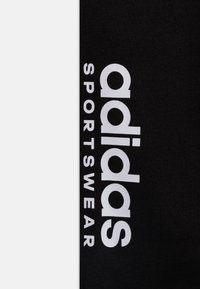 Černý sportovní materiál s výrazným bílým nápisem „adidas SPORTSWEAR“. Design zdůrazňuje moderní typografii na texturovaném povrchu.