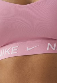 Sujeción deportiva rosa con una textura suave, que presenta una amplia banda elástica con el logo "NIKE" y suturas sutiles.