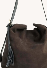 Sac seau en daim marron avec une texture douce, présentant une large ouverture, une fine sangle en cuir et un accent à pompon sur le côté.