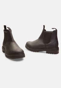 Las botas de tobillo de cuero negro cuentan con paneles laterales elásticos, punta redondeada, suela de goma gruesa y tiradores en la parte posterior para facilitar su uso.