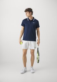 Dunkelblauses Polo-Shirt mit weißem Kragen, weiße Shorts und weiße Sportschuhe. Hält einen Tennisball und einen Schläger. Schlichtes, funktionales Design.
