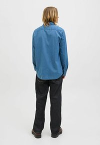 Denimskjorta i medelblå, långärmad med knappmanschetter, figursydd passform, rundad nederkant och en yokesöm bak; matchad med mörka byxor.