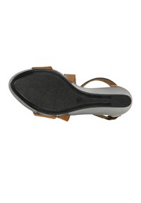 Sandale en cuir marron avec une semelle en caoutchouc noir texturé, dotée d'un talon plat et de sangles ajustables pour un maintien sécurisé.