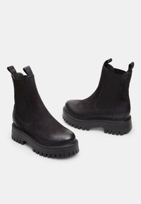 Botas Chelsea negras de cuero con paneles laterales elásticos, lengüetas de tirón y suelas de goma gruesa con profundas estrías.