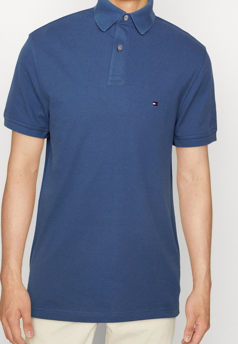 Polo bleu en coton, doté d'un col avec revers, de manches courtes et d'un petit logo sur le côté gauche de la poitrine. Texture lisse.