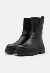 Botas cortas de cuero negro con punta redondeada, textura suave, cierre lateral con cremallera y suela gruesa de goma negra.