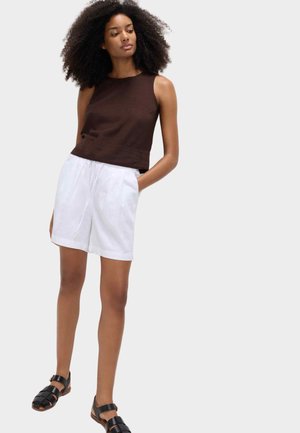Top marrón sin mangas combinado con pantalones cortos blancos. Los pantalones cortos tienen cintura con cordón y bolsillos laterales. Sandalias negras con tiras completan el conjunto.