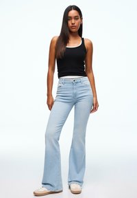 Svetlo modre široke kavbojke, kombinirane s črno oprijeto majico brez rokavov. Tkanina je videti mehka, z gladko teksturo in subtilnimi detajli na žepih.