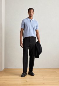 Polo de color azul claro con mangas cortas, pantalones negros y zapatos negros. Corte ajustado, diseño liso, con un pequeño logo en el pecho.
