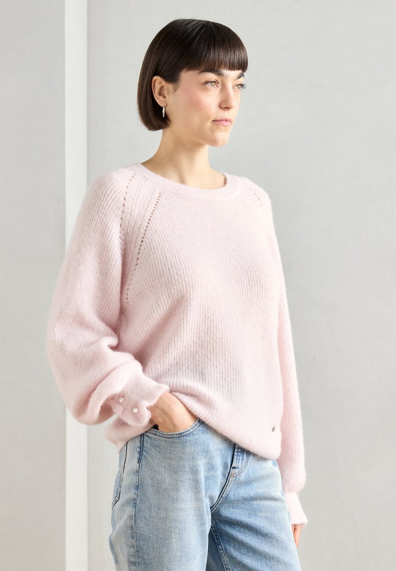 Light pink, knit sweater with a crew neck, ribbed texture, and soft, voluminous sleeves. Features pearl button accents on the cuffs.