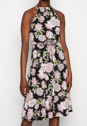 Halternek zwarte jurk met roze en witte bloemenprint, tailleceintuur gestrikt, knielengte, gedragen door persoon met een donkere huidtint.