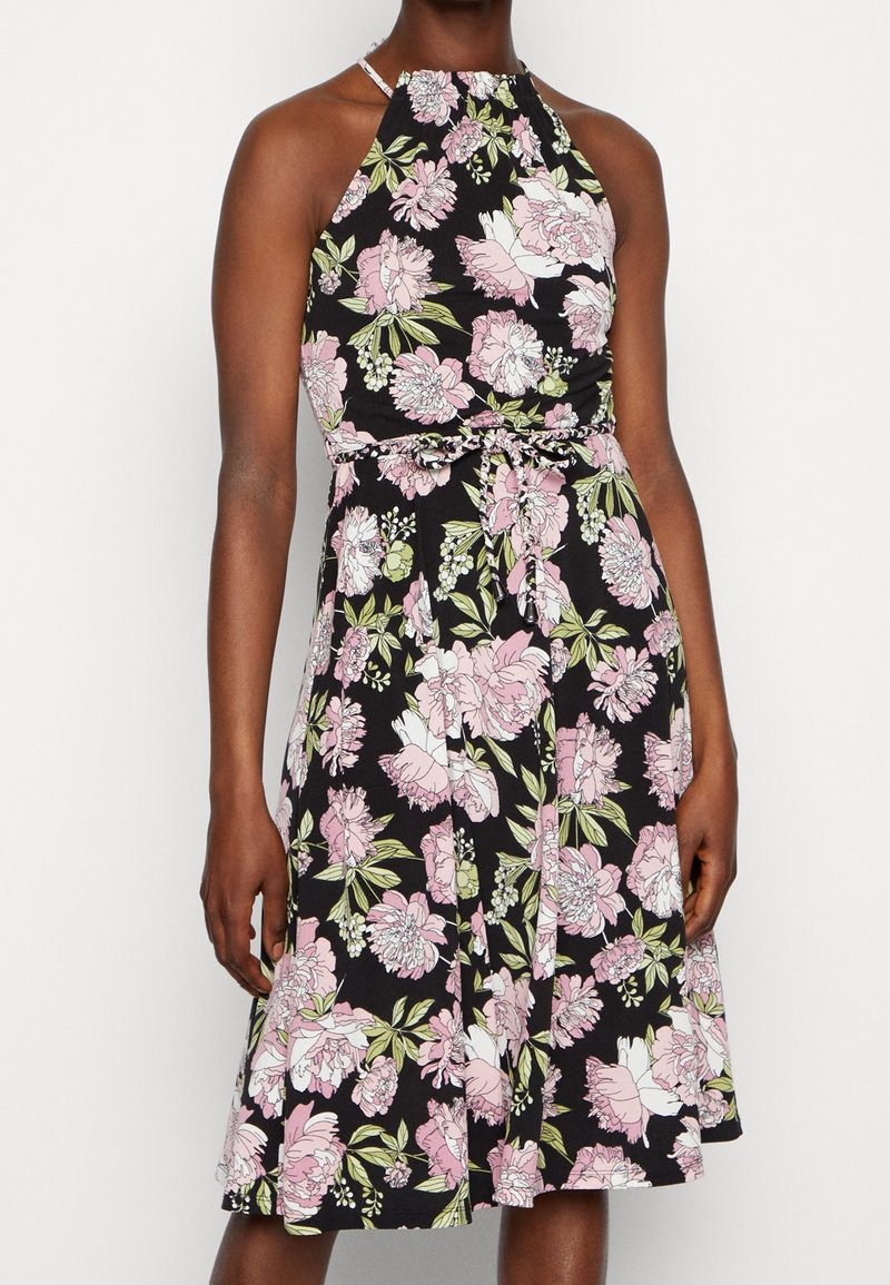 Robe noire à col licou avec imprimé floral rose et blanc, ceinture nouée à la taille, longueur au genou, portée par une personne à la peau foncée.