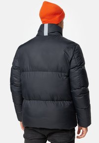 Puffervinterjakke i mørk navy med høj krave og reflekterende stribe, med kviltede sektioner. Bæret med en orange strikket hue.