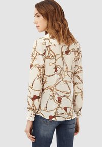 Blusa de manga larga en tejido crema con un estampado de cadena y borlas, con detalles en los puños y un corte relajado. Combinada con jeans de denim.