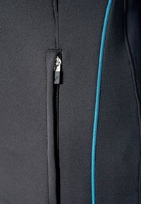 Giacca sportiva nera con tasca con zip, texture liscia e cuciture a contrasto color teal lungo il lato.