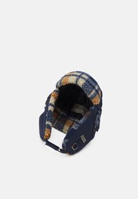 Marineblauwe hoed met een zachte, geruite, wollen voering in blauw, oranje en crème. Voorzien van een knoop en een verstelbare band aan de zijkant.