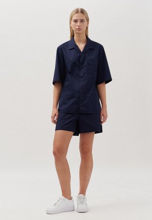 Chemise bleu marine à manches courtes et short assorti en tissu léger, avec une poche avant et une coupe décontractée, associés à des baskets blanches.