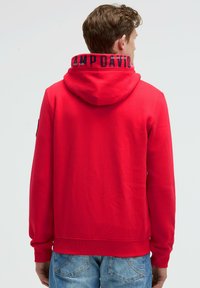 Sudadera con capucha roja que presenta un logotipo negro impreso en el cuello, mangas largas y una tela suave y texturada.