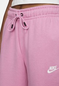 Rosa Nike sweatpants med dragsko i midjan, med svart metall, mjuk tygkänsla och en vit logotyp på vänster lår.