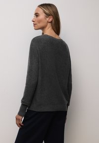 Pull gris en tricot avec une coupe ample, un col rond et des manches longues. Tissu texturé et doux avec des accents côtelés aux poignets et à l'ourlet.