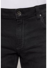 Schwarze Jeans aus Denim mit Knopfverschluss, slim fit, sichtbaren Nähten und einer leicht ausgewaschenen Textur im Bereich der Taschen.