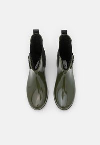 Stivali alla caviglia in gomma verde con finitura lucida, foderati in tessuto nero e dotati di anelli per la presa sul tallone. Forma elegante e dettagli di design minimal.