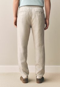 Lyse beige linnedbukser med en afslappet pasform, elastisk talje og to baglommer. Tekstureret overflade og subtil glans.