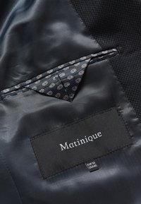 Sötétkék dzseki bélés mintás zsebkendővel és egy fekete címkével, rajta a "Matinique" felirattal, EUR 50 US 40 mérettel.