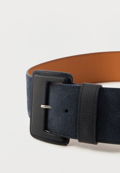 Μαύρη δερμάτινη ζώνη με μεγάλο υφασμάτινο ορθογώνιο αγκράφα και σκούρο υφασμάτινο λουράκι, μερικώς τυλιγμένη σε λευκό φόντο.