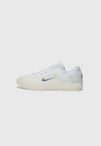 Baskets blanches avec une semelle en caoutchouc lisse et une tige en mesh, présentant un logo Nike bleu évasé sur le côté et un talon texturé.