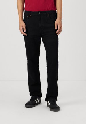 Sorte denim jeans med rett passform, fem lommer og subtile sømdetaljer, brukt med en rød T-skjorte og svarte joggesko.
