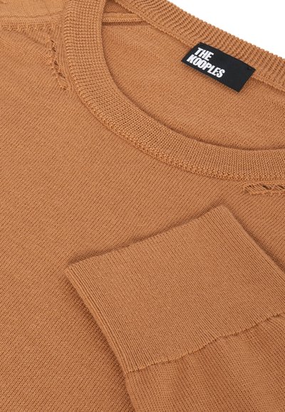 Pull en tricot marron avec un col rond, présentant des coutures visibles et une finition texturée. Étiquette : "THE KOOPLES." Pas de détails supplémentaires.