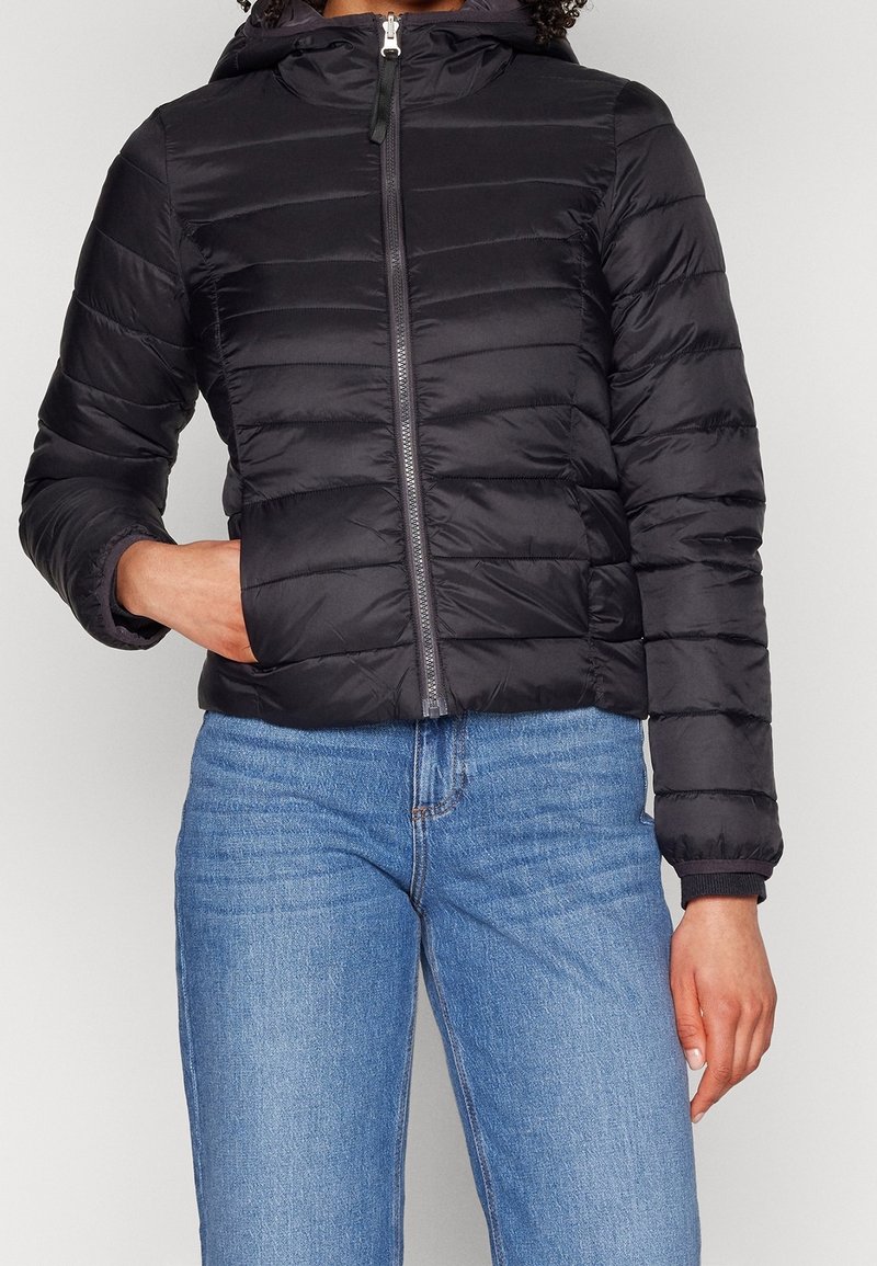 Sort polstret jakke med hætte, der har vandrette sømme og en frontlynlås, parret med lyseblå jeans. Teksturen fremstår glat.