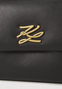 Borsa a tracolla nera in pelle con un logo dorato prominente, texture liscia, design elegante e chiusura a patta senza hardware aggiuntivo.