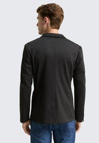 Ciemnoszara marynarka wykonana z fakturowanej tkaniny, z wąskim klapem i dopasowanym krojem, zestawiona z niebieskimi jeansami.