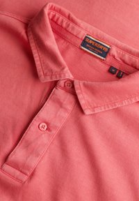 Polo shirt rosa con colletto classico, placket con due bottoni e dettagli del tag. Realizzato in tessuto morbido con una texture liscia.