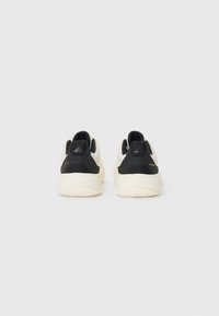 Weiße und schwarze Sportschuhe mit einem strukturierten Stoff-Obermaterial, schwarzen Fersenkappen und einer flexiblen Gummisohle. Mit Logo-Details.