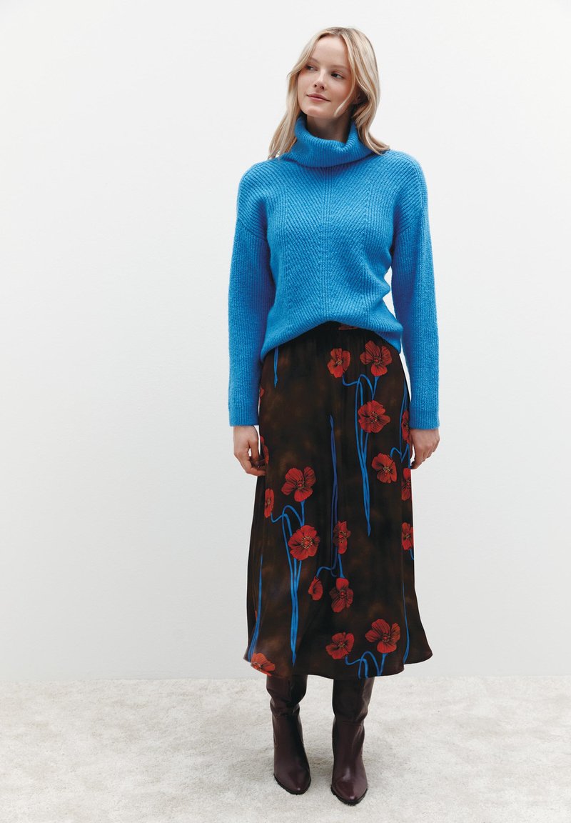 Blauer Strickpullover mit Rollkragen und strukturiertem Muster, kombiniert mit einem braunen Midirock mit Blumenmuster, der rote Blumen und blaue Stängel zeigt, abgerundet mit braunen Absatzstiefeln.