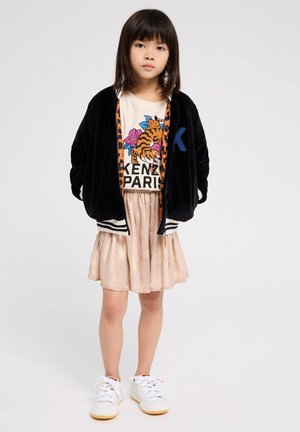Zwarte fluwelen bomberjack met witte strepen, grafisch T-shirt met een tijger en bloemen, gelaagd met een lichtroze textuurskirt en witte sneakers.