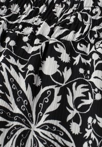 Tissu noir avec motifs floraux et feuilles blancs, ainsi que des plis horizontaux texturés sur la partie supérieure.