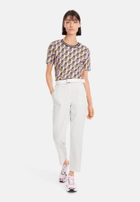 Kurzärmliges, rosa Hemd mit Ananas-Muster und schwarzem Kragen, kombiniert mit weißen Hosen und rosa Turnschuhen.