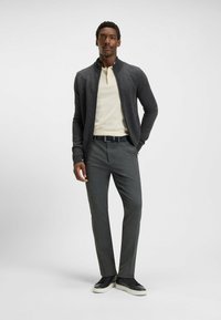 Gray zip-up cardigan over a cream polo, paired with gray tailored trousers and black sneakers with white soles. Smooth textures and streamlined fit.