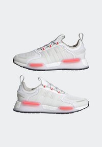 Vita sportskor med meshuppbyggnad, grå accenter, röd dämpning och svart gummisula. Har snören och öglor vid hälen för enkel påtagning.