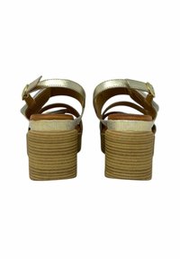 Sandali con tacco oro metallizzato, dotati di due cinturini regolabili, con una suola a pianta piatta in morbido marrone chiaro e una fodera interna liscia.