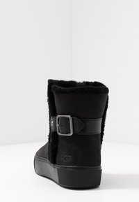 Bottine en daim noir avec doublure en fausse fourrure et semelle en caoutchouc plate. Présente une sangle en cuir noir avec un détail de boucle en argent.