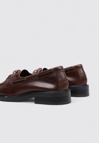 Zapatos de cuero marrón con una textura lisa, punta redonda, diseño con cordones y un tacón bajo de goma negra. Ojales reforzados y detalles de costura.