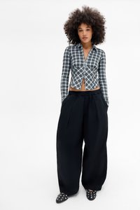 Čierno-biely karovanový crop top s dlhými rukávmi, spárovaný s voľnými čiernymi nohavicami a čiernymi slip-on topánkami so študmi.
